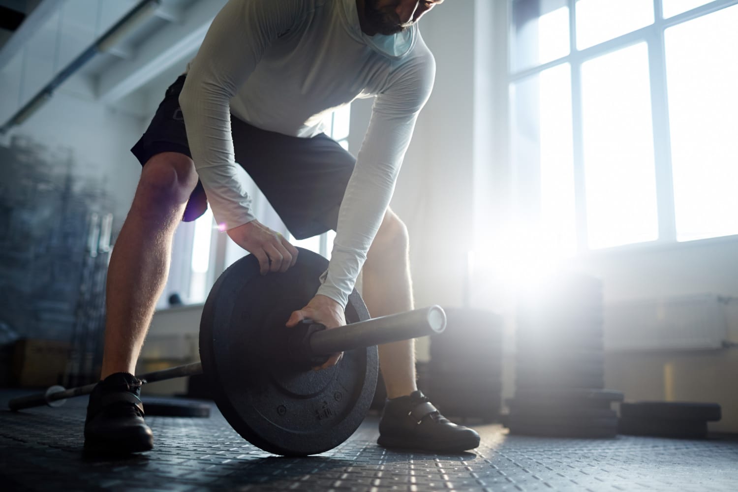 Man loading a weight plate onto a barbell in a sunlit gym