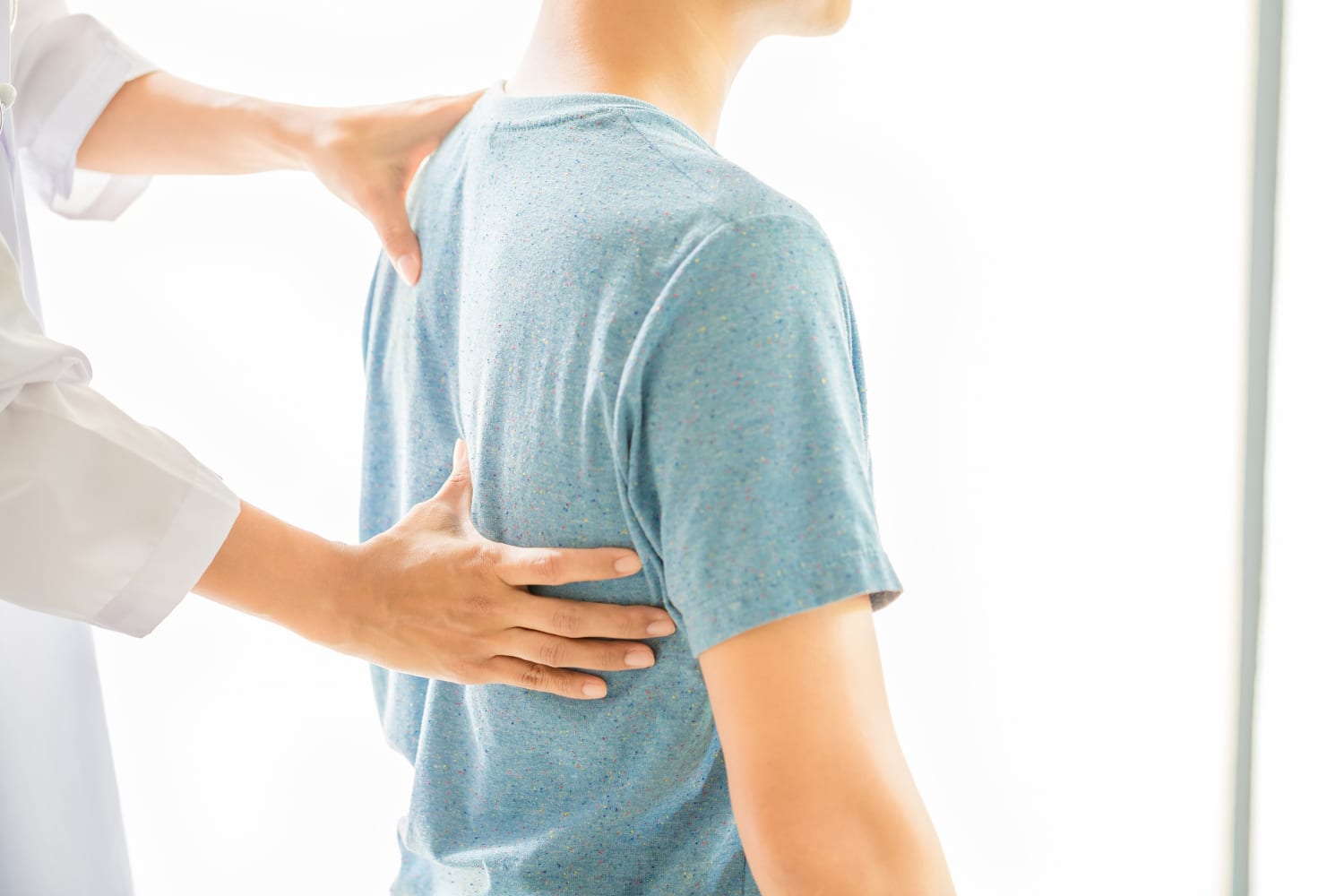 Clinician checking a man's back posture with hands on his shoulder blade and ribs