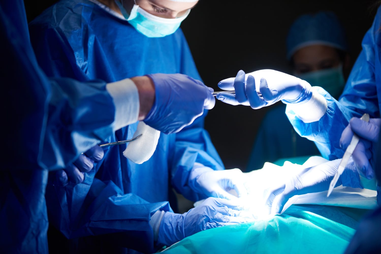 Surgical team passing instruments over a patient during an operation