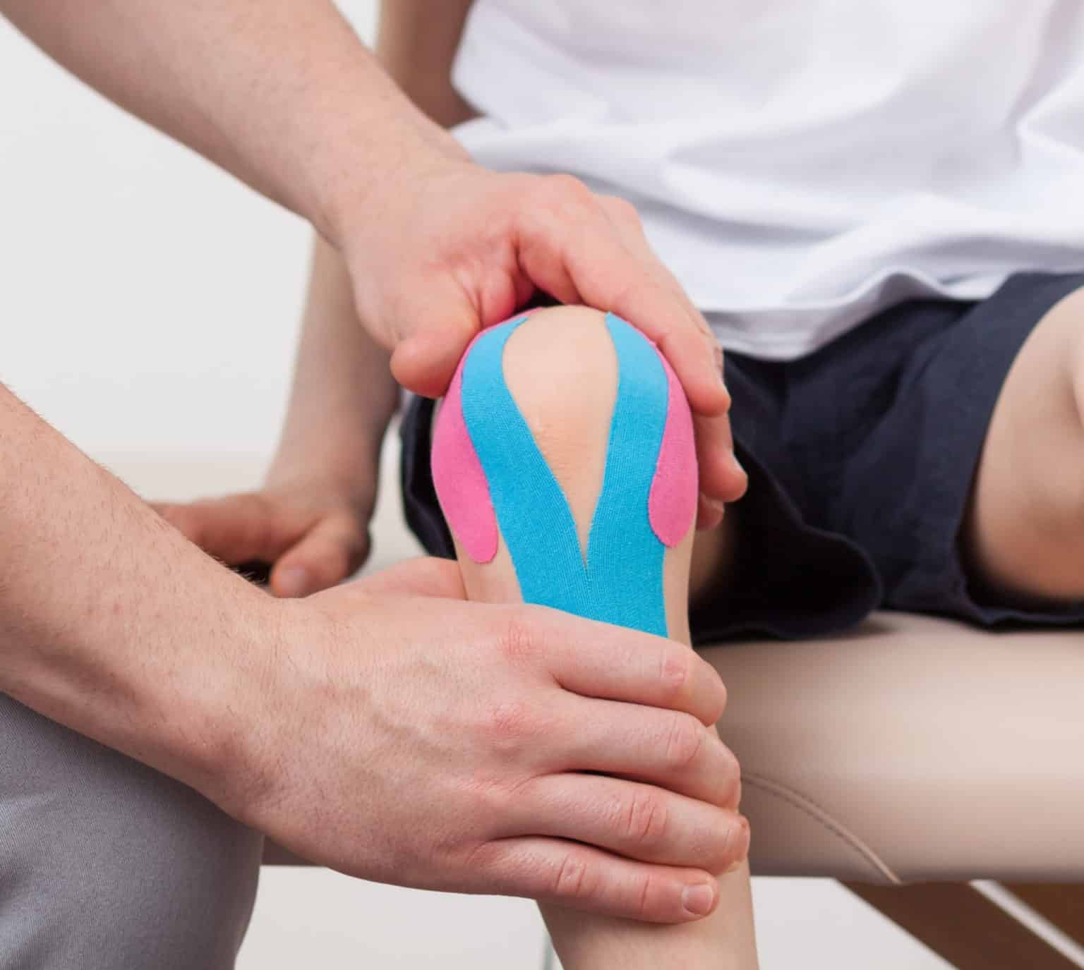 Physical therapist holding a patient's knee wrapped in blue and pink kinesiology tape