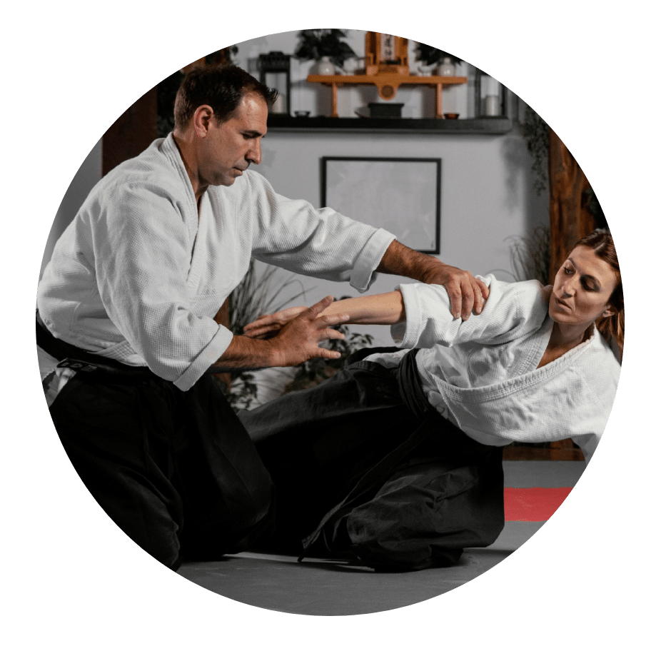 Martial arts instructor in a gi controlling a training partner's arm on the mat