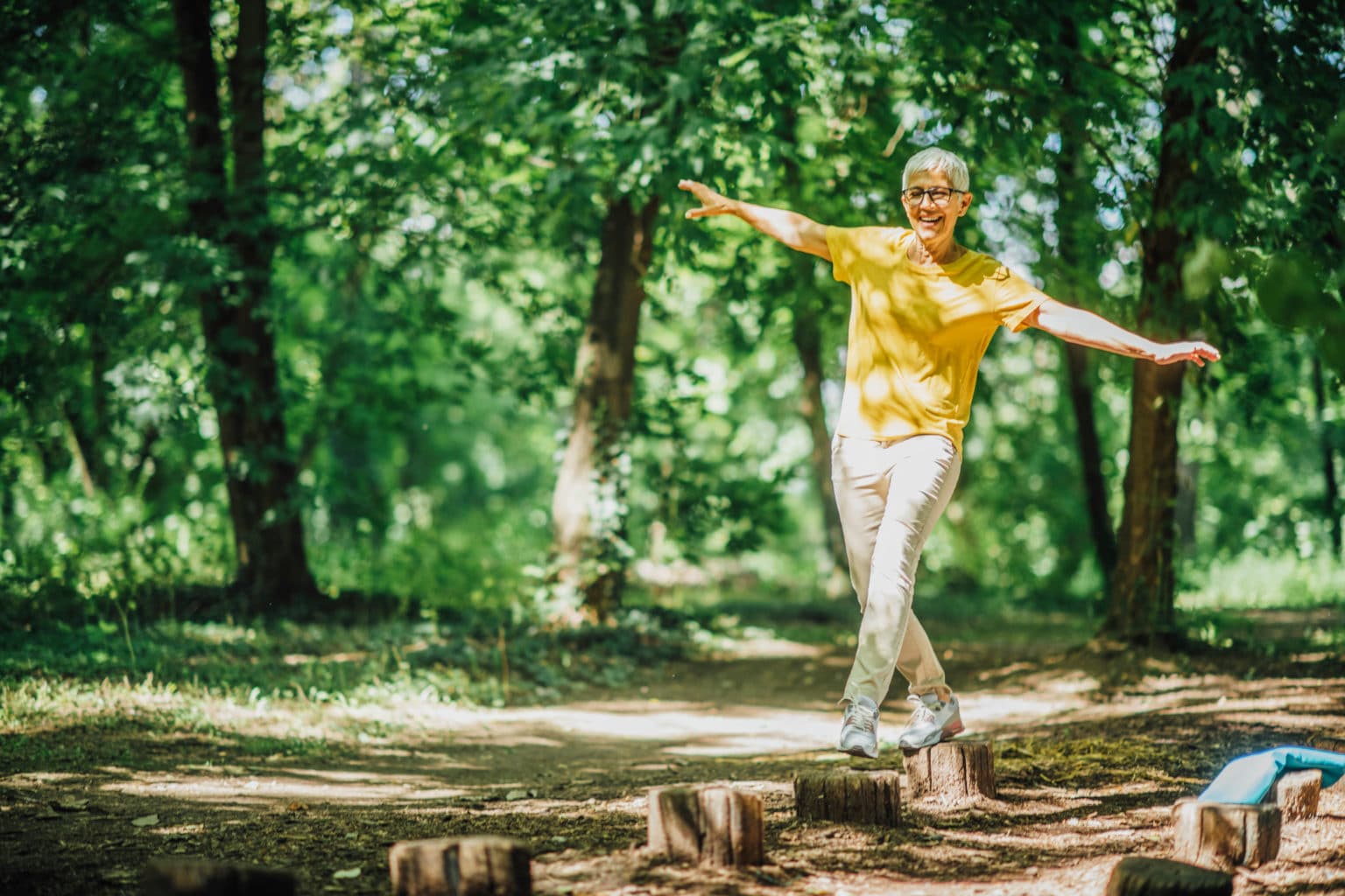 Woman practicing balance by stepping across tree stumps with her arms out