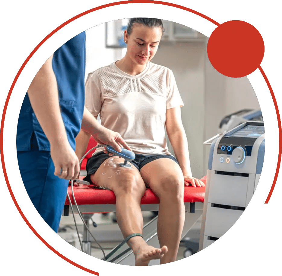 Physical therapist treating a seated woman's knee with a handheld therapy device